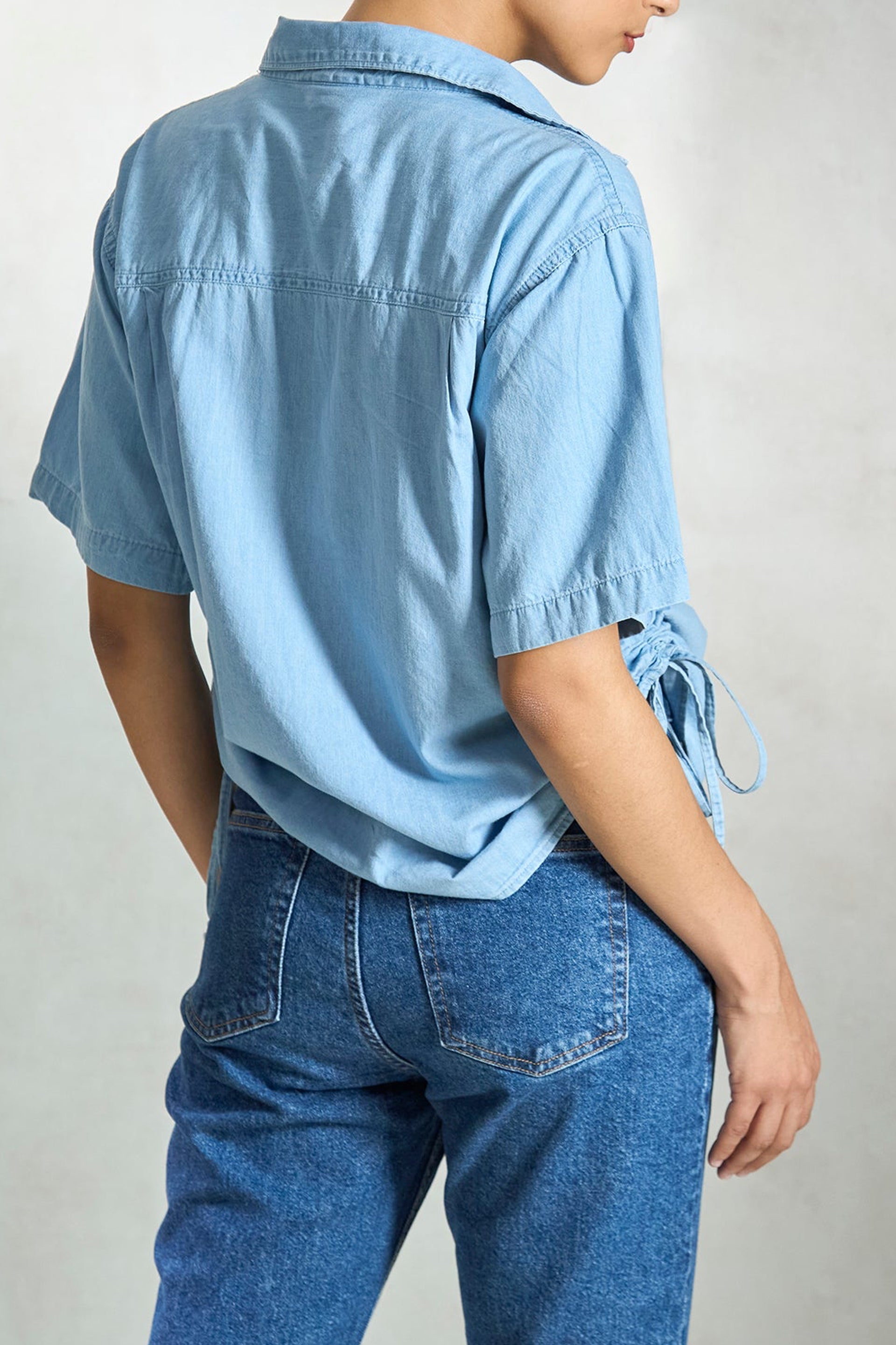 Light blue denim drawstring shirt with short sleeves and tie details at the sides