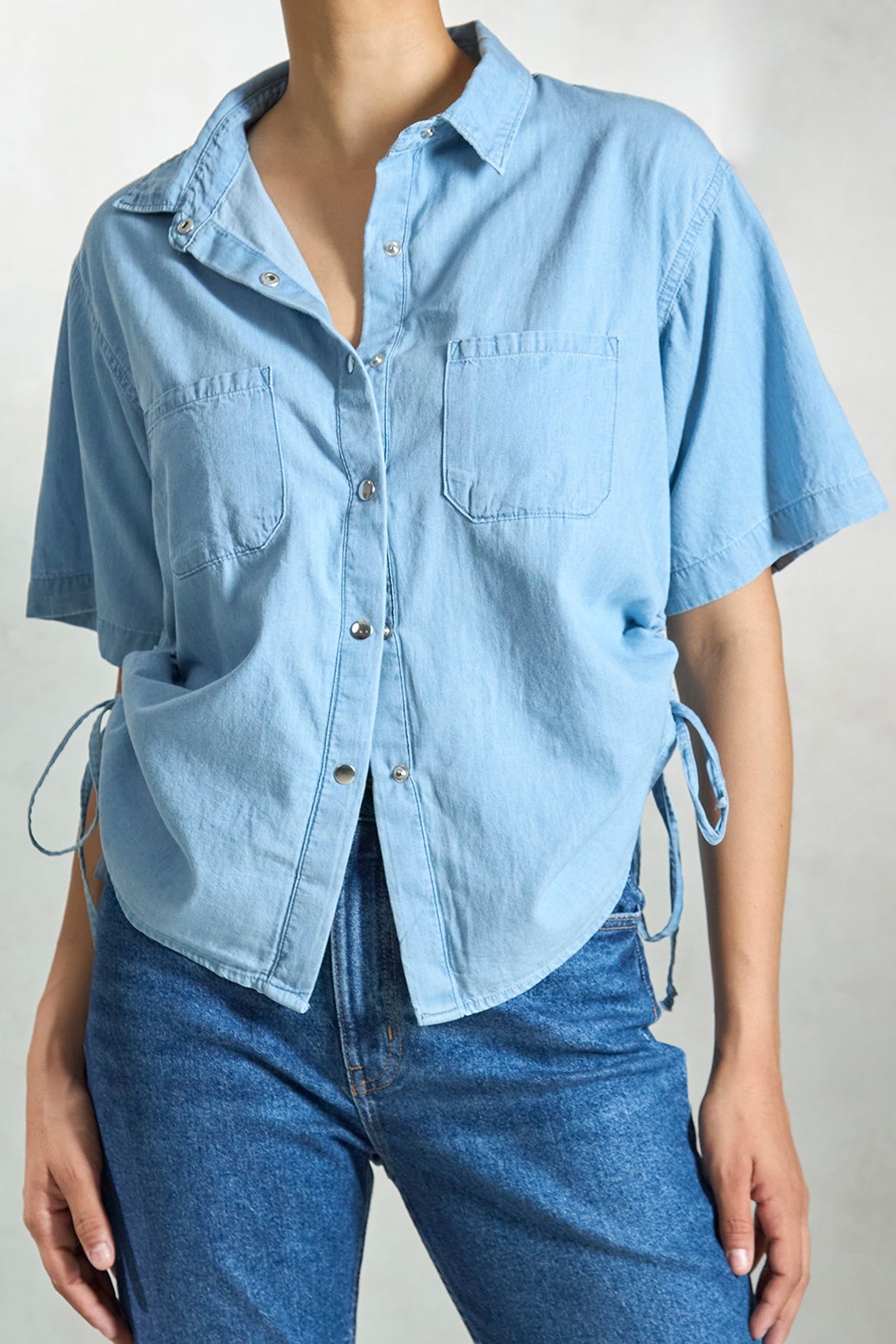 Light blue denim drawstring shirt with short sleeves and side ties for a relaxed fit