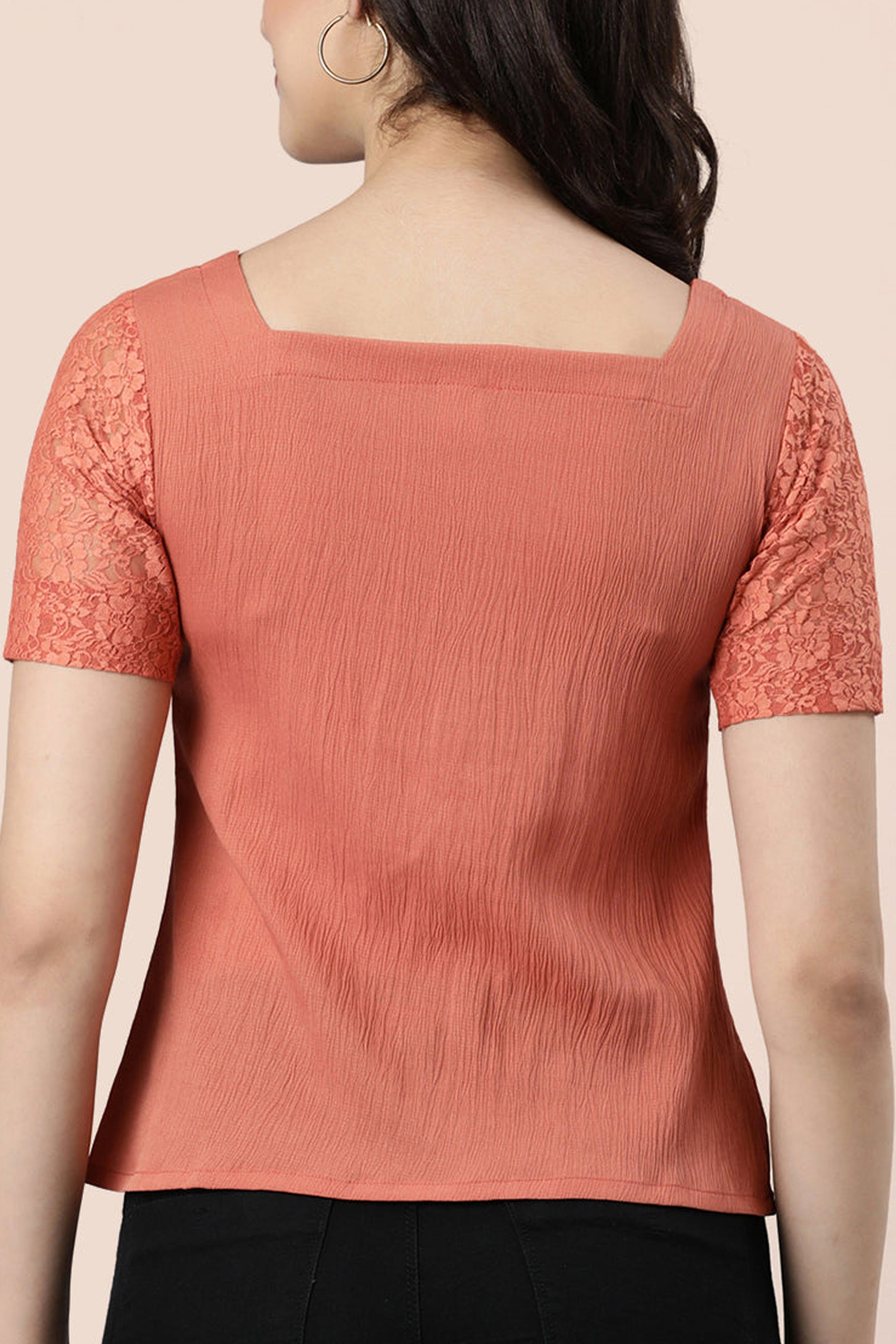 Back view of a rose gold lace top featuring short lace sleeves and a textured front