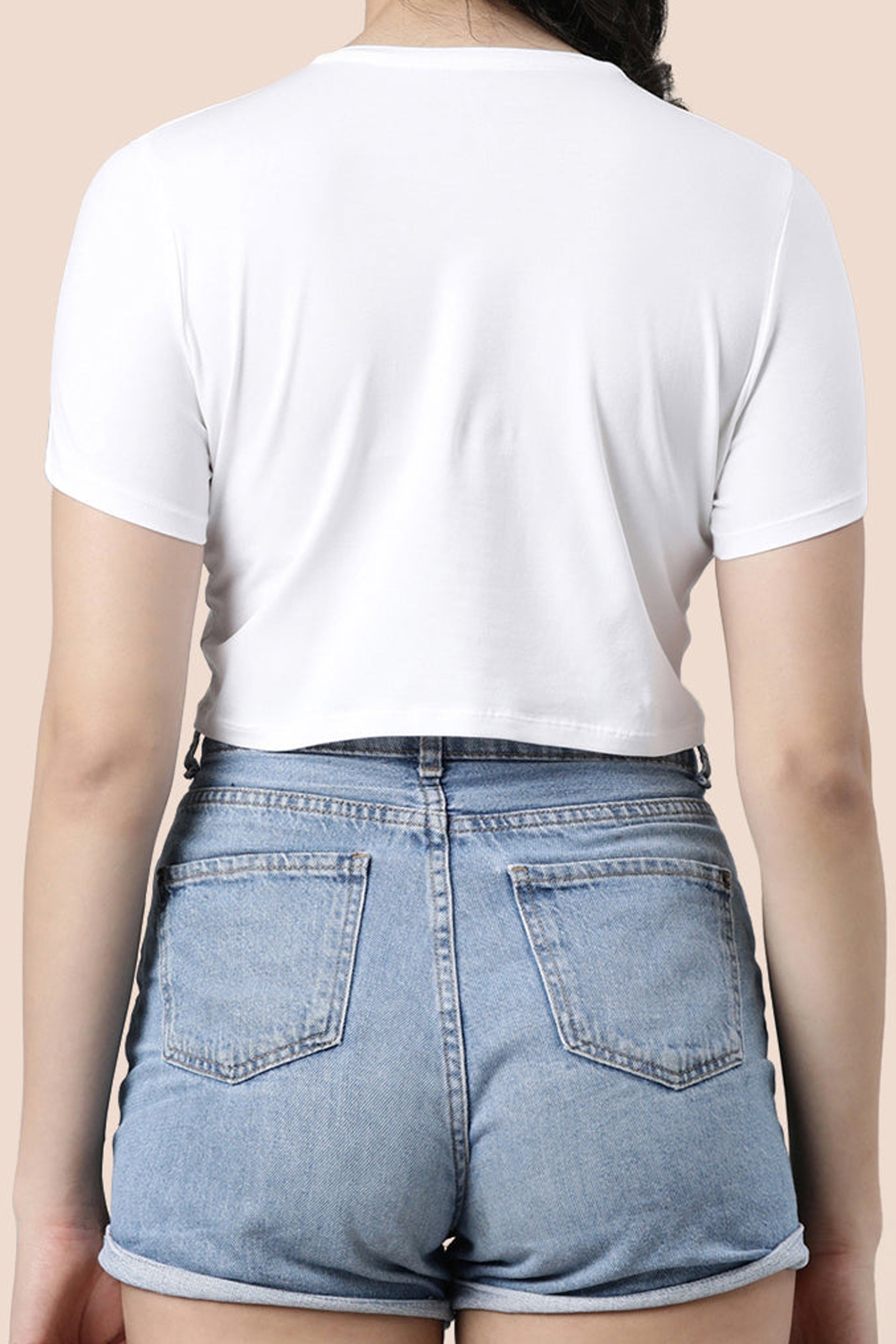 Back view of a woman wearing a white crop top for women paired with denim shorts