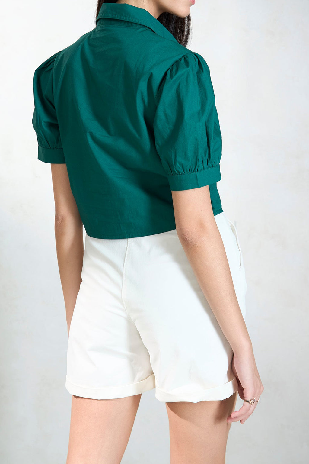 Back view of a green women's puff sleeve blouse styled with white shorts
